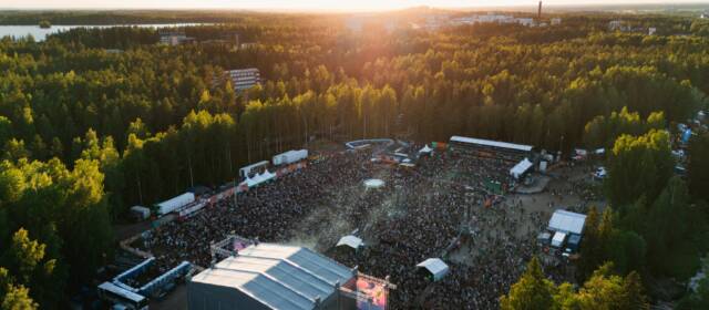 Ilmakuva Provinssista, päälavan yläpuolelta. Aurinko paistaa, paljon asiakkaita ja Provinssin myyntipisteitä, taustalla vehreää metsää ja rakennuksia.